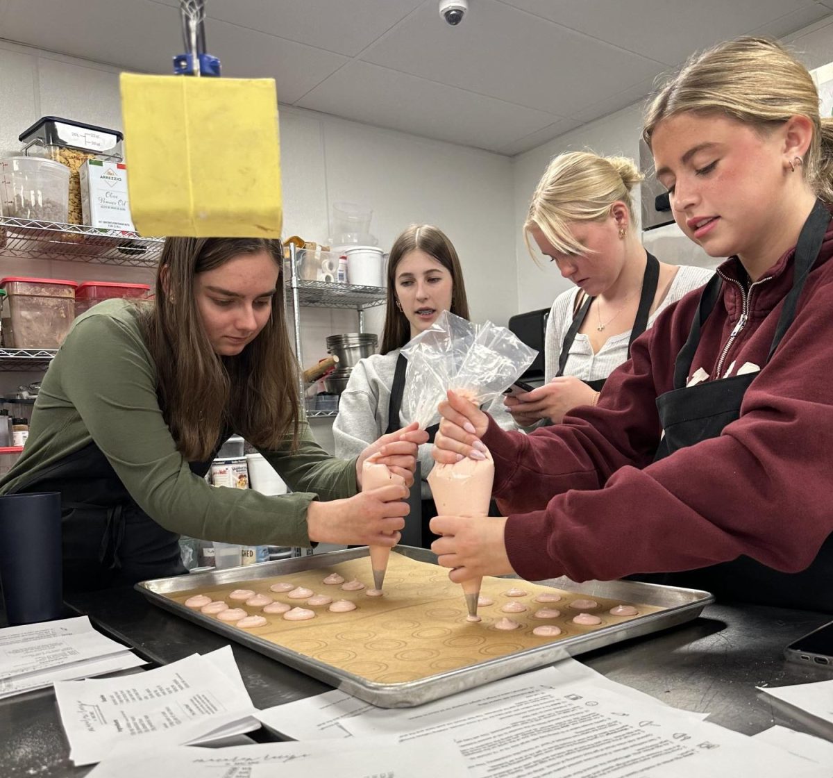 French Club members Bakers piping macaron batter to bake.
Bakers filling their baked macarons with buttercream frosting.